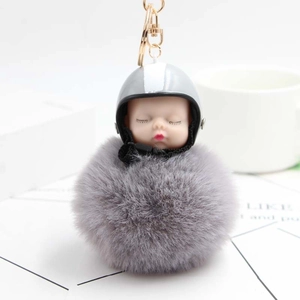 Detail of grey fluffy pompom keychain with mini motorcycle helmet and sleeping baby doll