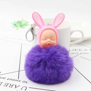 Detail of creative sleeping baby doll with rabbit ears and a purple fluffy fur ball charm