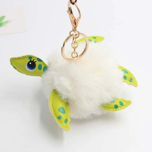 Detailed view of turtle plush keychain with white faux fur pompom and green spotted fins