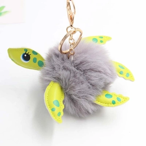 Close-up of plush turtle keychain with grey faux fur ball and green spotted limbs