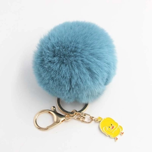 Dettaglio portachiavi a pompon blu con chiusura dorata e ciondolo a forma di papera gialla