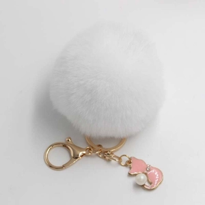 Detail of white faux fur pompom keychain with golden lobster clasp and pink enamel fox charm