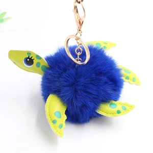 Close-up of fluffy blue turtle plush keychain with green polka dot limbs and golden clasp