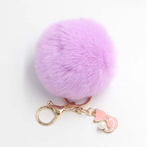 Plush purple pompom keychain with gold fox charm and pearl accent on white background