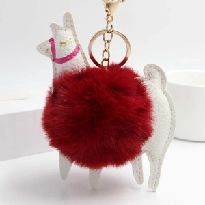 Detail of alpaca plush keychain with deep red fur ball and white leather texture