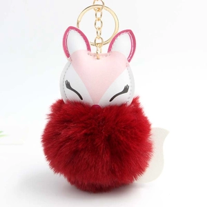 Detail of cute sleeping fox keychain with burgundy faux fur pom-pom and golden hardware