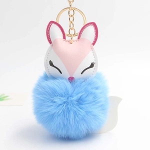 Close-up of sleeping fox charm with soft blue pom-pom and gold metal keychain