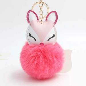 Close-up of sleeping fox keychain with pink fluffy pom pom and golden ring clasp