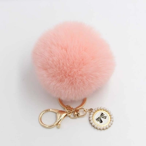 Close-up of pink faux fur ball keychain with golden metal ring and bow pearl pendant
