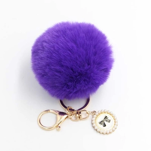 Detailed shot of dark purple plush pompom keychain with golden bow and pearl charm