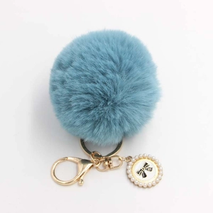 Close-up of blue faux fur pompom keychain with golden clasp and pearl bow charm