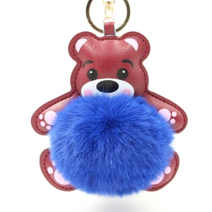 Detail eines roten Bären-Schlüsselanhängers mit blauem Plüsch-Pompon und Goldring