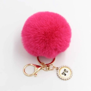 Detail of rose red fluffy pompom keychain with golden bow charm and pearl inlay