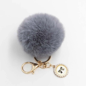 Detail of grey faux fur pom pom keychain with gold clasp and pearl bow charm