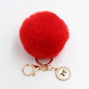 Detail of red faux fur pompom keychain with golden clasp and pearl bow charm