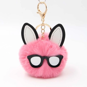 Detail of pink faux fur rabbit pompom keychain with chic black round glasses and gold hardware
