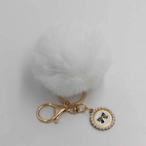 Detail of white fluffy pompom keychain with gold hardware and pearl bow charm