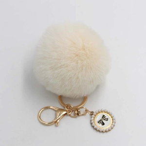 Detailed view of fluffy cream faux fur pompom keychain with pearl bow pendant