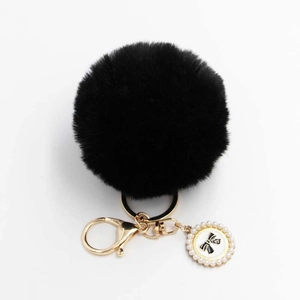 Detail of black plush pompom keychain with golden lobster clasp and pearl bow charm