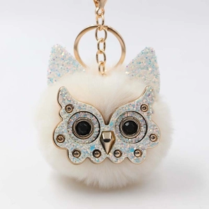 Close-up of white plush owl keychain with sparkling gold metal face and crystal eyes
