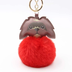 Detail of red plush ball keychain with a brown leather dog charm and gold metal ring
