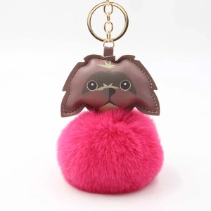 Close-up of fluffy magenta faux fur pom-pom with brown leather puppy charm and gold keychain