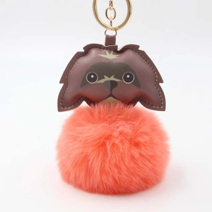 Close-up of fluffy orange pom-pom puppy keychain with brown leather details and gold ring