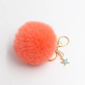 Plush coral pom pom keychain with gold ring and blue starfish charm on white backdrop