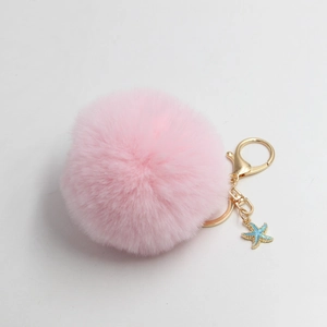 Detailed close-up of pink faux fur pompom keychain with golden clasp and blue starfish charm