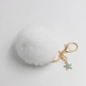 Detailed macro view of a fluffy white pom pom keychain with gold clasp and blue starfish charm