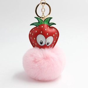 Detail view of a strawberry plush keychain with a soft pink faux fur ball and gold metal ring