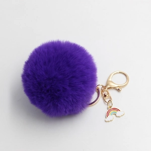 Detail view of purple faux fur pompom keychain with a golden clasp and rainbow charm