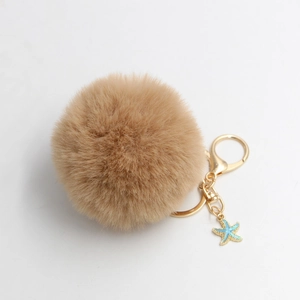 Detail of soft beige faux fur pompom keychain with golden clasp and blue starfish charm