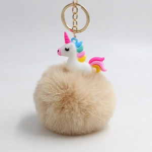 Dettaglio di un pompon in finta pelliccia con ciondolo a unicorno e portachiavi d'oro