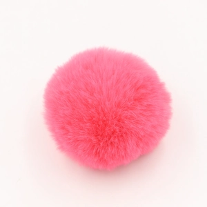 Dettaglio di un pompon in finta pelliccia rosa brillante soffice con trama in fibra morbida