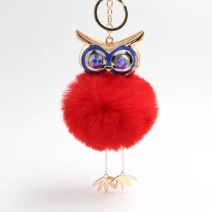 Detail of owl plush keychain featuring a bright red faux fur pompom and gold metal owl head