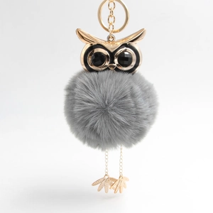 Macro detail of plush owl keychain with gray faux fur ball and golden metal owl head charms
