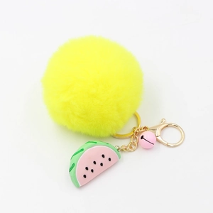 Détail d'un porte-clés pompon jaune en fausse fourrure avec breloque pastèque et clip doré