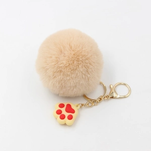 Détail d'un porte-clés pompon en peluche, chaîne dorée et pendentif en forme de patte