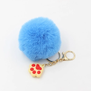 Détail du porte-clés pompon bleu avec fermoir doré et pendentif en forme de patte
