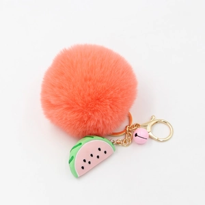 Détail d'un porte-clés pompon en fausse fourrure orange corail avec breloque pastèque et cloche