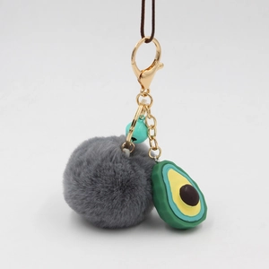 Plush avocado keychain with dark grey pompom and blue bell on gold lobster clasp