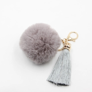 Détail d'un porte-clés boule en peluche gris-violet avec pompons et fermoir doré