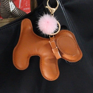 Brown leather dog keychain with pink fur pompom on black bag, gold lobster clasp detail