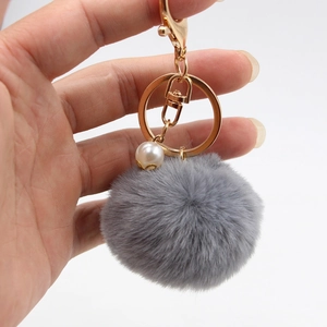 Close-up of grey faux fur pompom keychain with golden clasp and decorative pearl