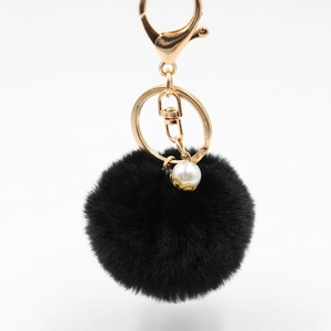 Detail of a black plush pompom keychain with golden lobster clasp and pearl accent charm