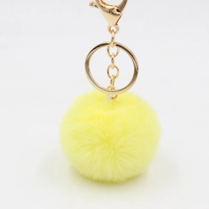 Détail d'un porte-clés pompon jaune moelleux avec anneau doré et fermoir mousqueton