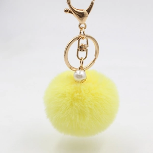 Close-up of lemon yellow plush ball keychain with gold hardware and a pearl bead accent
