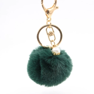 Detail of dark green faux fur pompom keychain with golden clasp and white pearl charm