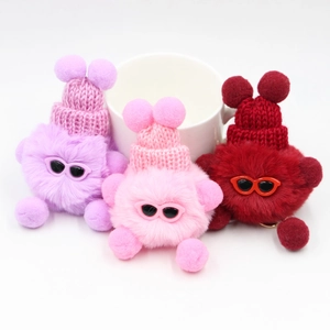 Trois porte-clés pompons en peluche avec bonnets en tricot et lunettes sur fond blanc